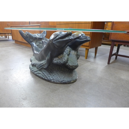 130 - An oval glass topped coffee table, on faux bronze dolphin base