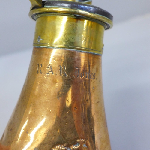 652 - A brass and copper powder flask with embossed scene, marked R.A.R. Jones