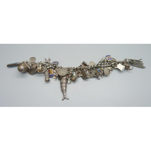 948 - A heavy silver charm bracelet with approximately 55 silver and white metal charms including drilled ... 