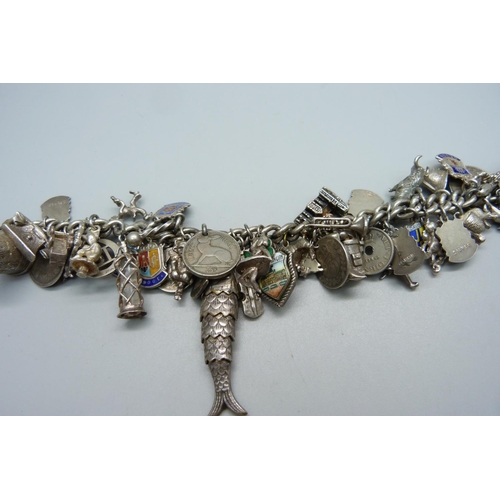 948 - A heavy silver charm bracelet with approximately 55 silver and white metal charms including drilled ... 