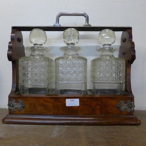 366 - An early 20th Century oak tantalus, with three glass decanters