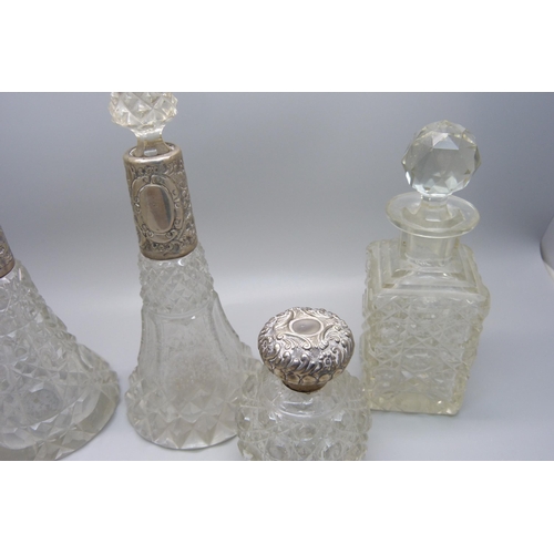 868 - A collection of five cut glass scent bottles with silver tops/collars, a small porcelain silver topp... 