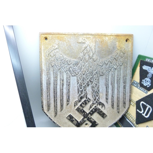 831 - A German WWII metal plaque, cap, mounted cloth badges, etc.