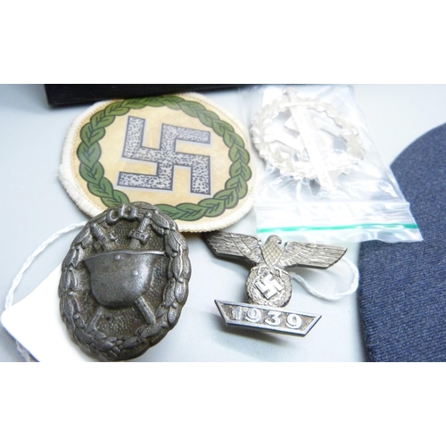 831 - A German WWII metal plaque, cap, mounted cloth badges, etc.