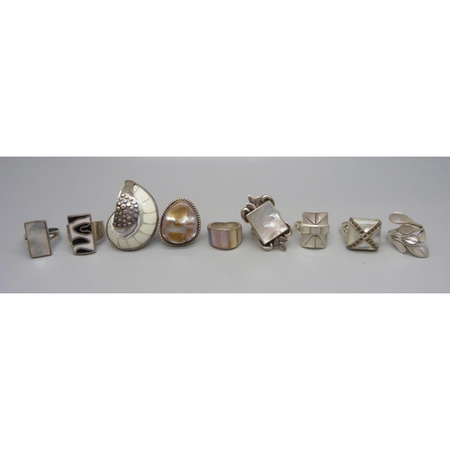 1054 - Eight chunky large silver rings set with mother of pearl, and one silver ring set with a fossil, 88g