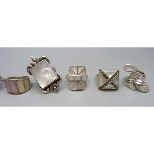 1054 - Eight chunky large silver rings set with mother of pearl, and one silver ring set with a fossil, 88g