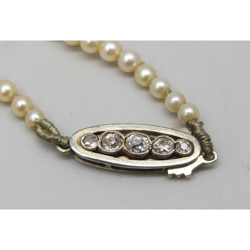 1024 - A cultured pearl necklace with a white metal five stone diamond clasp, circa 1930, approximately 45c... 