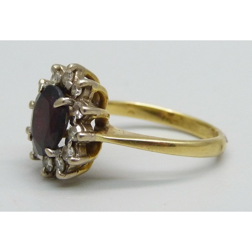 1047 - An 18ct gold ring set with a garnet and diamond halo, 4.3g, K