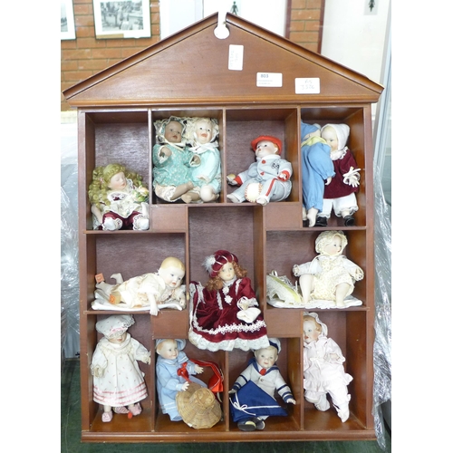 A doll display case with thirteen small china dolls and one other larger doll PLEASE NOTE THIS LOT