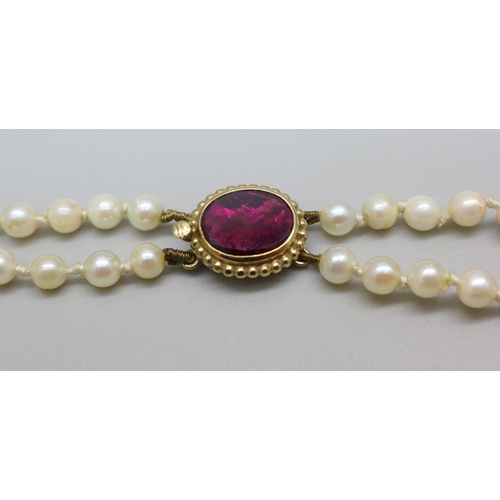 888 - A graduated double string pearl necklace, the yellow metal clasp set with a pink stone, tests as ame... 