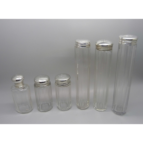 864 - Six silver topped glass bottles, five with monograms to lid