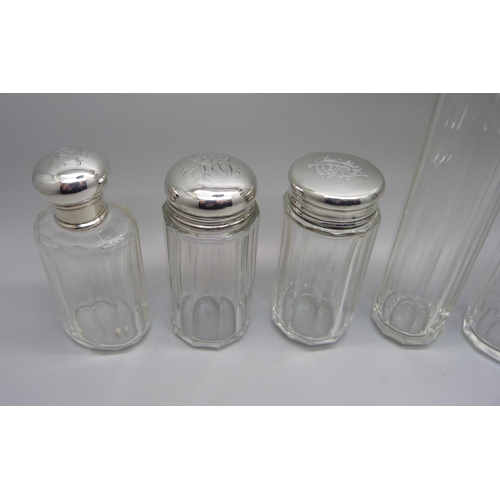 864 - Six silver topped glass bottles, five with monograms to lid