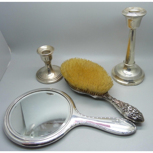 902 - Two silver candlesticks, a silver backed mirror and a silver brush