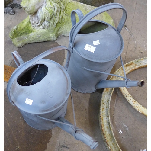 210 - A cast iron wheel crank and two galvanised watering cans