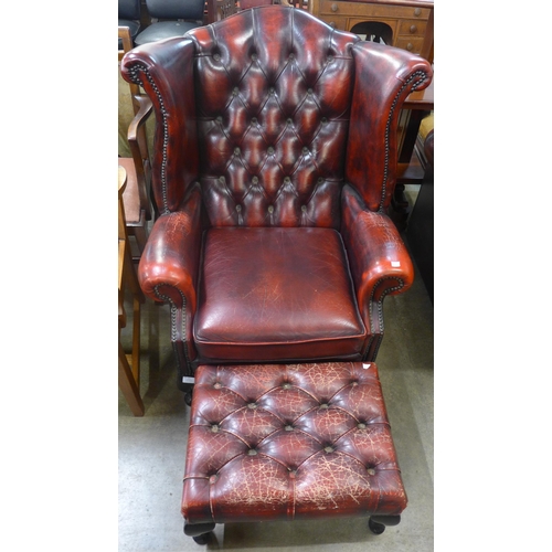 109 - An oxblood red leather Chesterfield wingback armchair and footstool