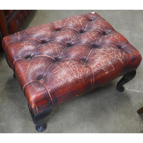 109 - An oxblood red leather Chesterfield wingback armchair and footstool