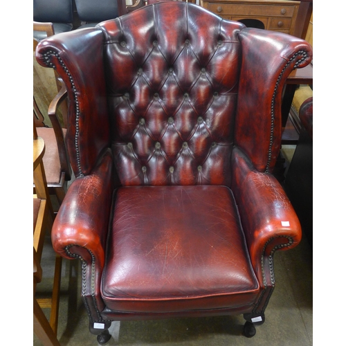 109 - An oxblood red leather Chesterfield wingback armchair and footstool