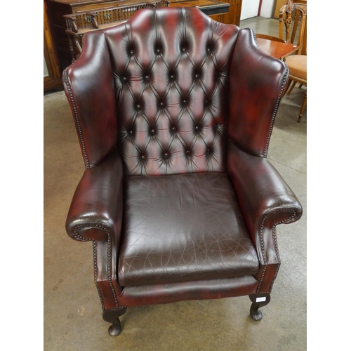 75 - An oxblood red leather Chesterfield wingback armchair