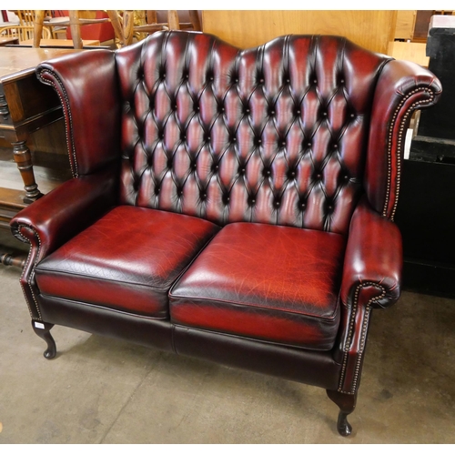 76 - An oxblood red leather Chesterfield wingback settee