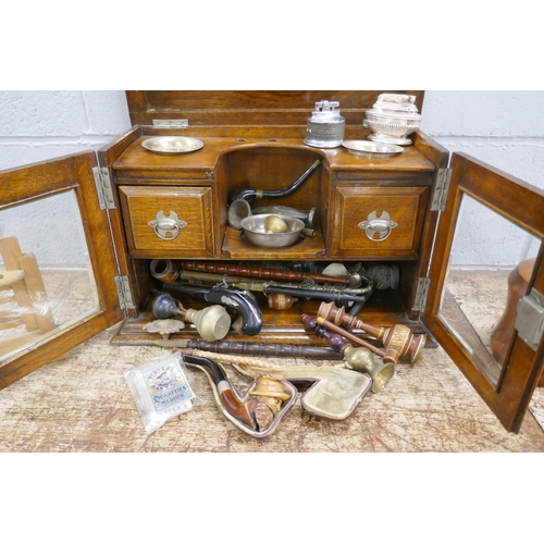 811 - An oak smokers cabinet with bevelled edge glass doors, a tobacco jar, a pipe rack and pipes