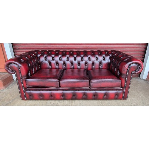 100B - An oxblood red leather Chesterfield three piece lounge suite, comprising, settee, club chair and sto... 