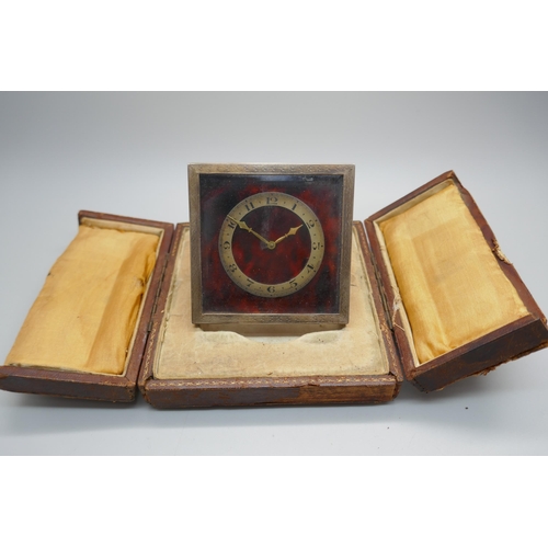 876 - A silver framed and tortoiseshell travel clock with bevelled glass, a Swiss made 8-day clock, the fr... 