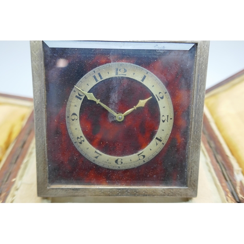 876 - A silver framed and tortoiseshell travel clock with bevelled glass, a Swiss made 8-day clock, the fr... 