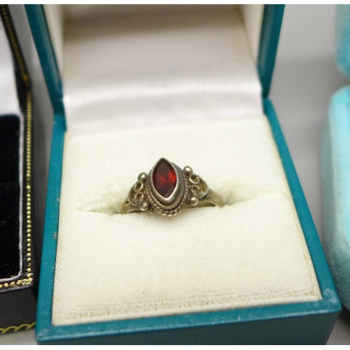 1061 - Six silver rings and one white metal ring set with a cabochon garnet, total weight 28g