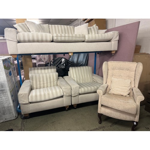 1544 - A cream fabric three piece suite comprising of a three seater sofa, two armchairs and a wingback cha... 