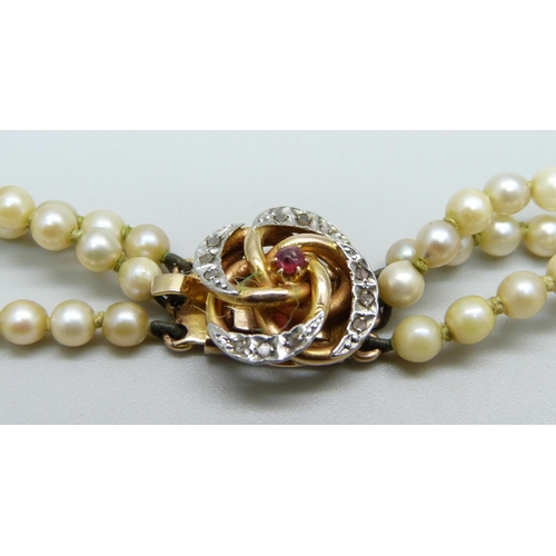 1013 - A three strand pearl necklace with a ruby and diamond clasp