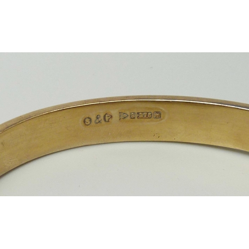 1042 - A 9ct yellow gold bangle with engraved front and safety chain, 9.9g