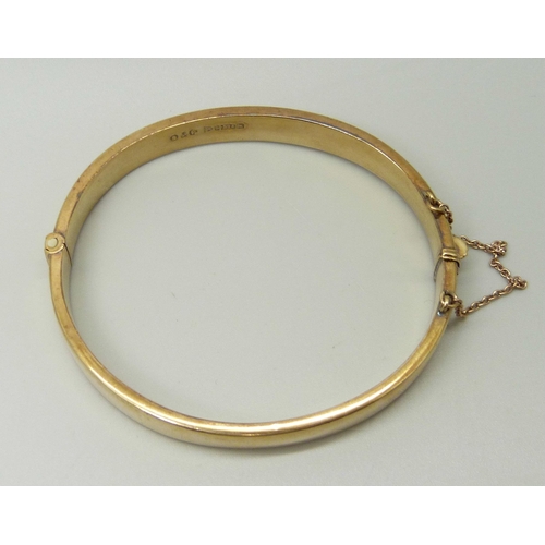 1042 - A 9ct yellow gold bangle with engraved front and safety chain, 9.9g