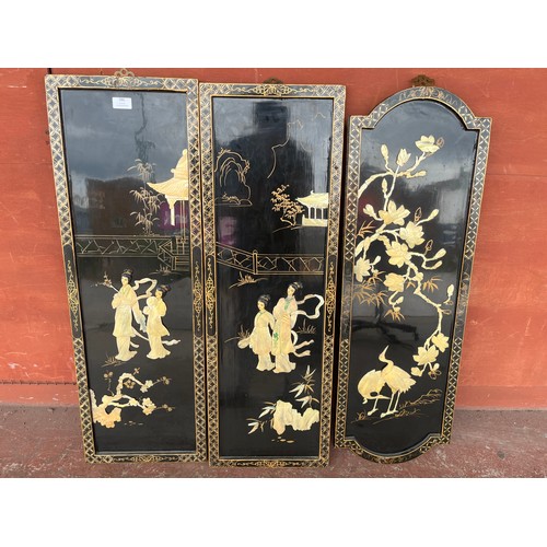 386 - A set of three Japanese black lacquered chinoiserie plaques, with faux shell relief decoration of fi... 