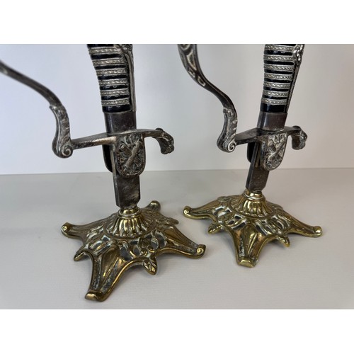 119 - A pair of brass mounted military sword handle candlesticks, 27cms h