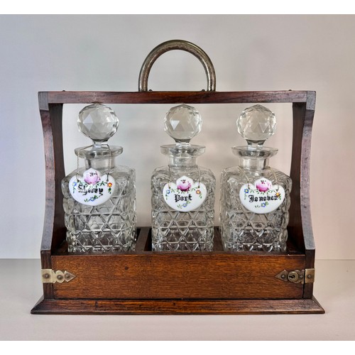 123 - An early 20th Century oak tantalus, with three glass decanters and porcelain spirit labels