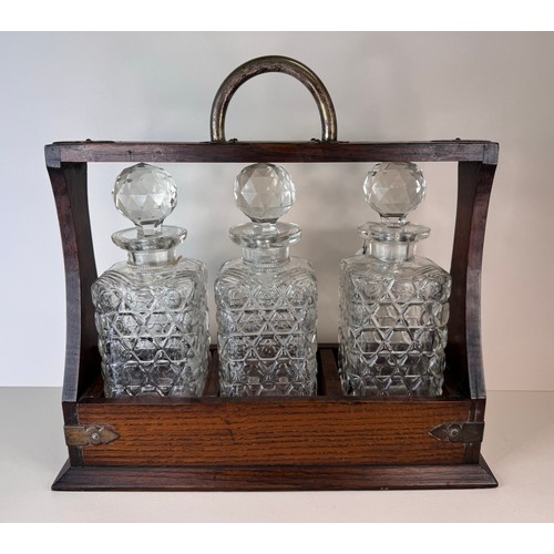 123 - An early 20th Century oak tantalus, with three glass decanters and porcelain spirit labels