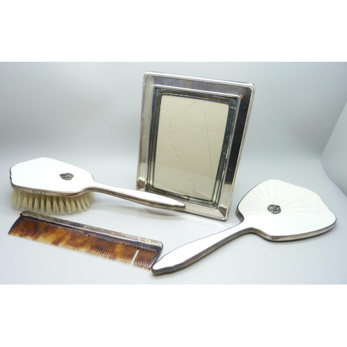 894 - A silver photograph frame, a silver and enamelled hand mirror and brush and a silver mounted comb