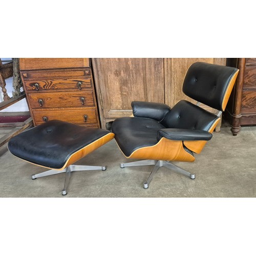 13 - A Charles & Ray Eames style simulated walnut and black leather revolving lounge chair and ottoman