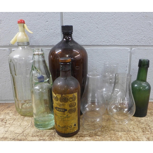 1056 - A box of glass bottles, chemist bottles, soda syphon and oil lamps and glass shades **PLEASE NOTE TH... 