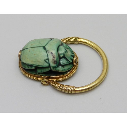 921 - An Egyptian yellow metal set scarab beetle ring with carved scene verso, 5.1g, size K