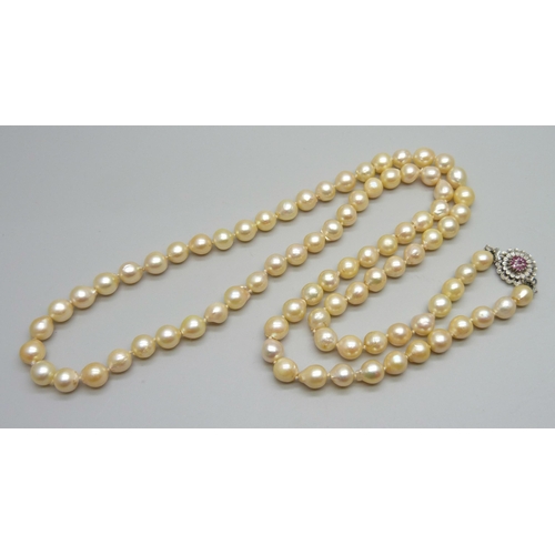 935 - A string of pearls with a white metal and ruby set flower cluster clasp, 76cm, 66g