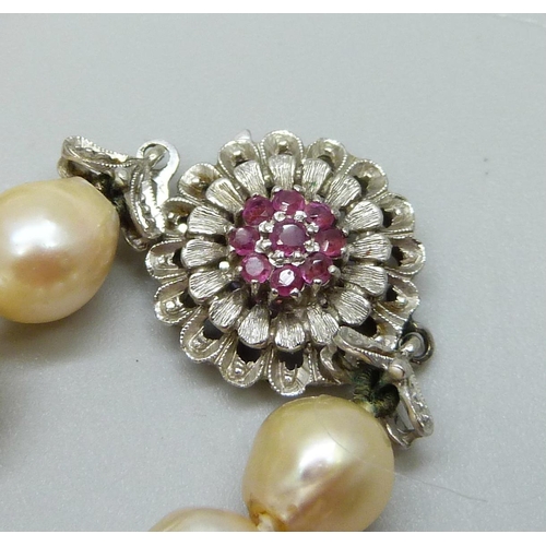 935 - A string of pearls with a white metal and ruby set flower cluster clasp, 76cm, 66g