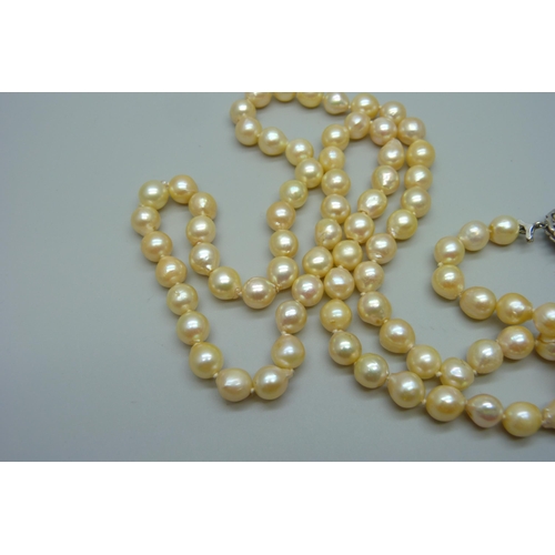 935 - A string of pearls with a white metal and ruby set flower cluster clasp, 76cm, 66g