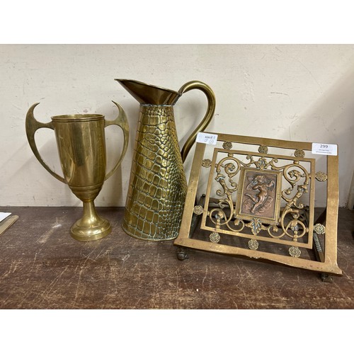 299 - A brass jug, two handled trophy/vase and a book stand with embossed copper plaque depicting a cherub