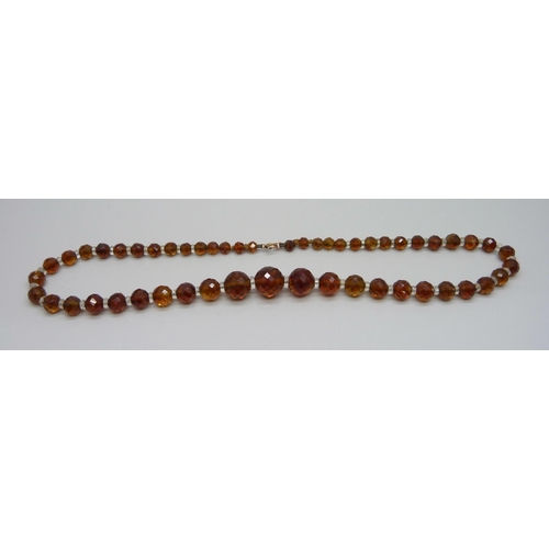 1139 - A string of amber coloured faceted glass beads with a yellow metal clasp, 49cm