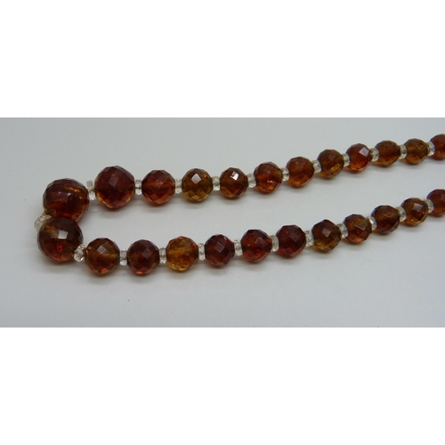 1139 - A string of amber coloured faceted glass beads with a yellow metal clasp, 49cm