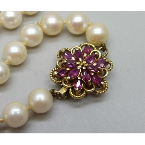 1067 - A string of cultured pearls with 14ct gold and ruby set clasp, 43g, 58cm