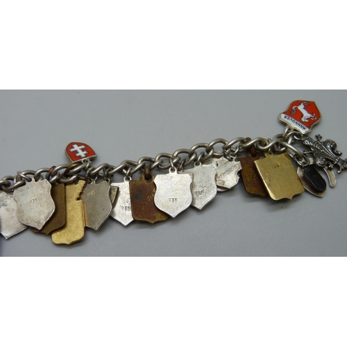 1043 - A white metal charm bracelet with enamel plaque charms including .835 silver and gilt metal, 53g tot... 