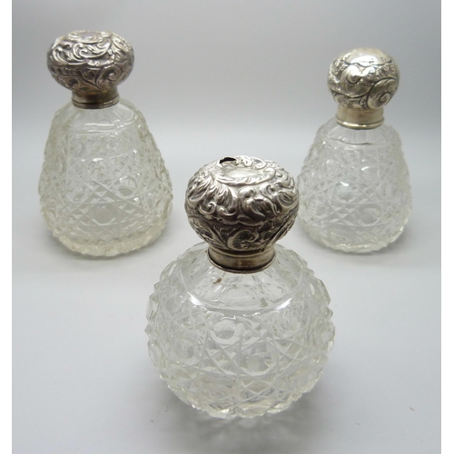 832 - Three cut glass silver topped early 20th Century scent bottles, two lacking stoppers and one without... 