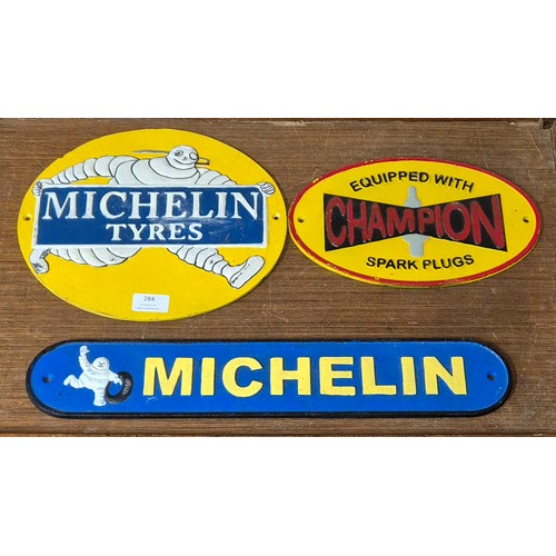 284 - Two cast iron Michelin advertising signs and a Champion spark plugs sign